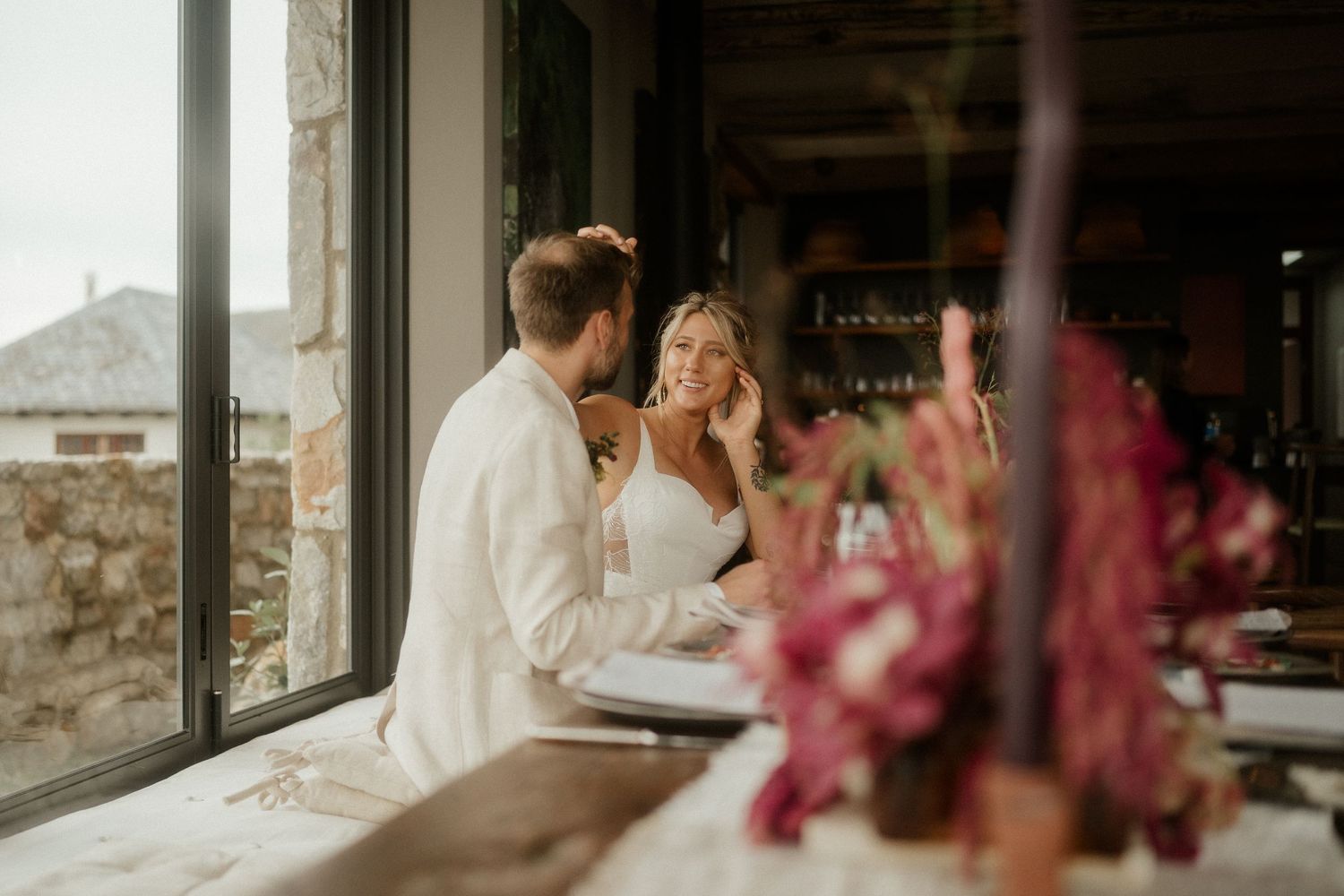 Couple sharing an intimate moment at a rustic venue with pink floral decorations in the foreground.
