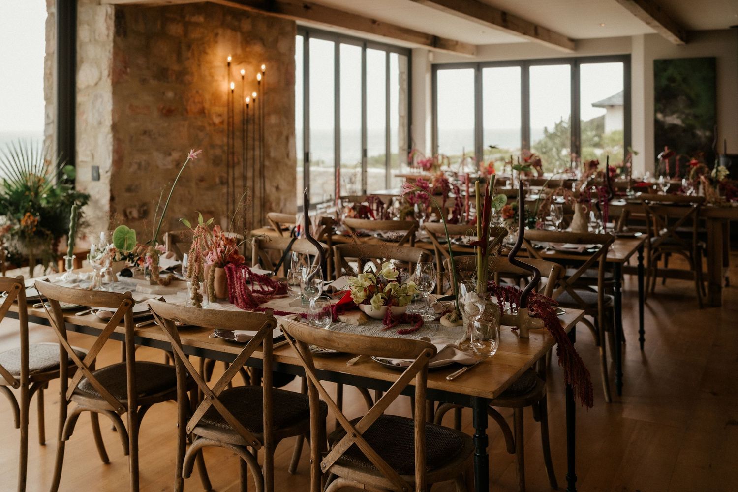 Rustic wedding reception venue with wooden tables decorated with floral centerpieces and place settings.