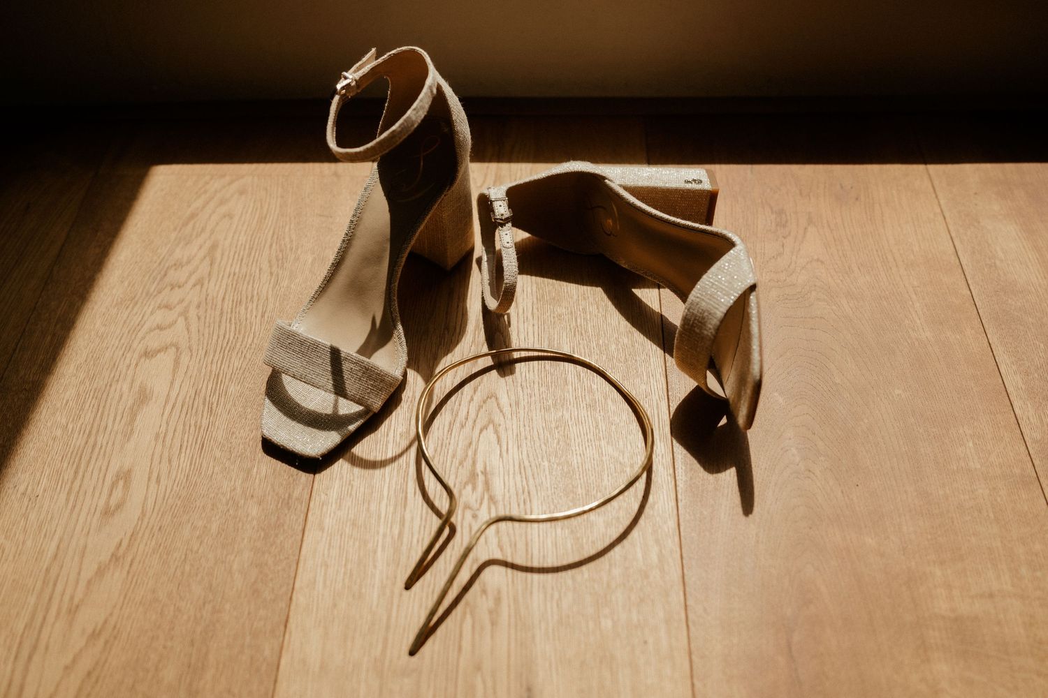 Wedding accessories including strappy heels and a hairpiece arranged on wooden flooring in dramatic lighting.