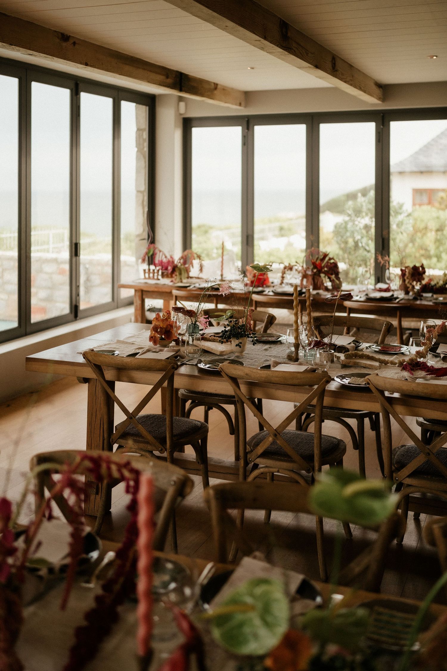 Rustic dining room with wooden tables, cross-back chairs and large windows overlooking scenic views, set for an elegant event.
