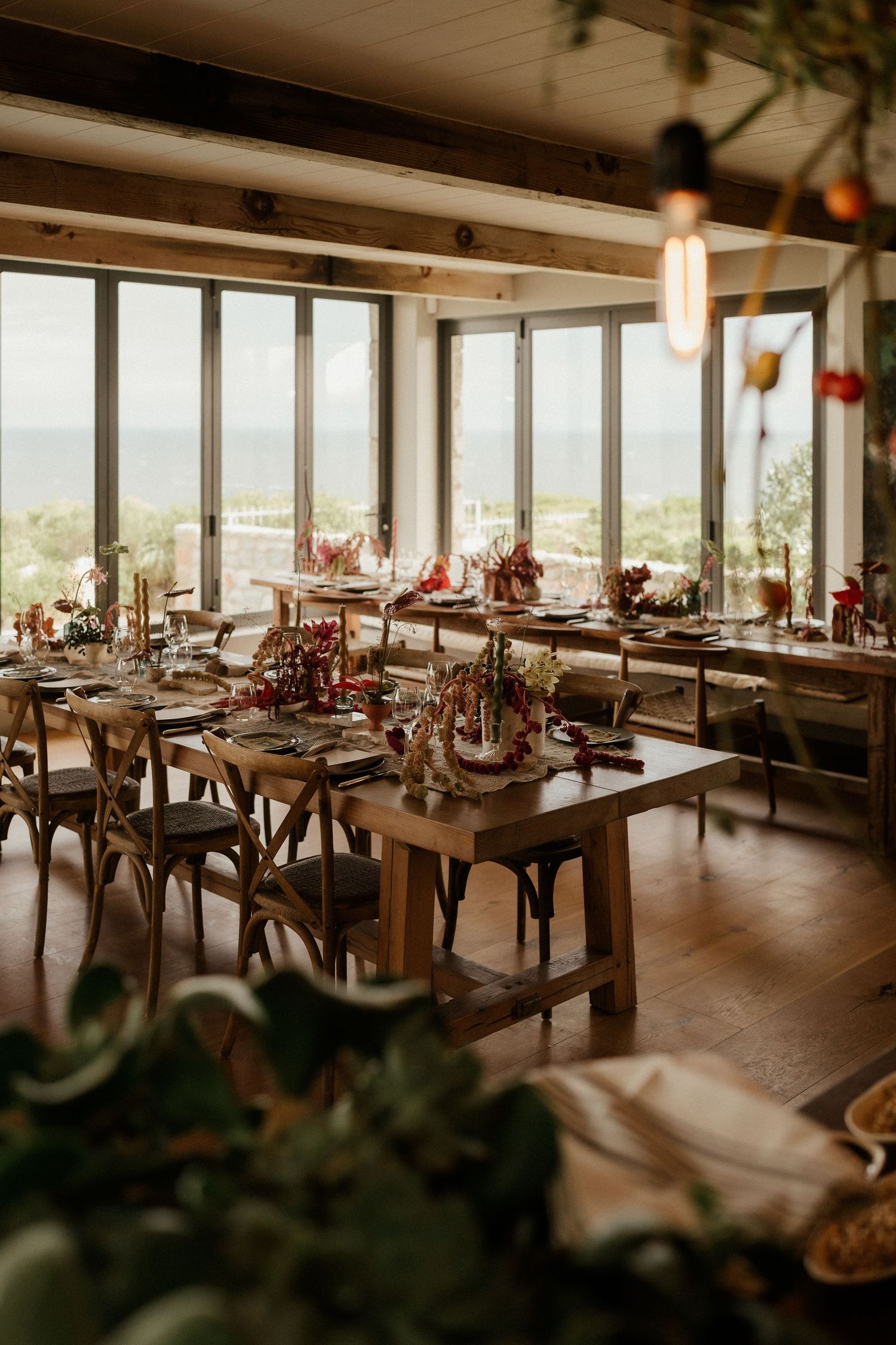 Elegant wedding reception dining room with ocean views and tables set with red floral centerpieces.