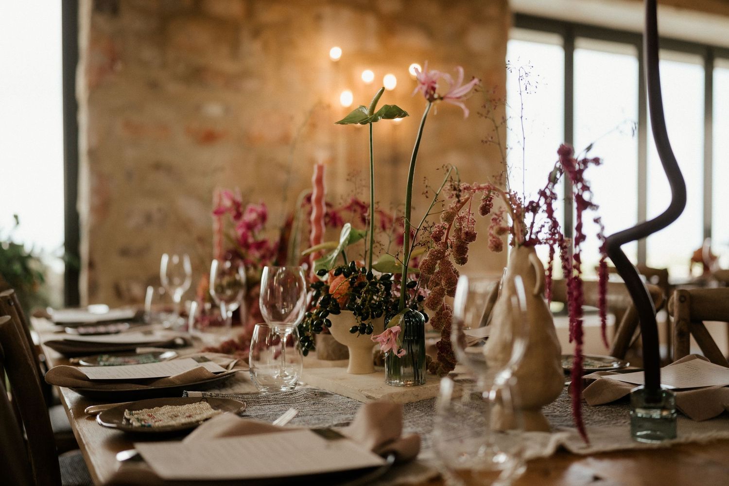 Elegant table setting with floral centerpieces and glassware in rustic indoor venue with stone walls.
