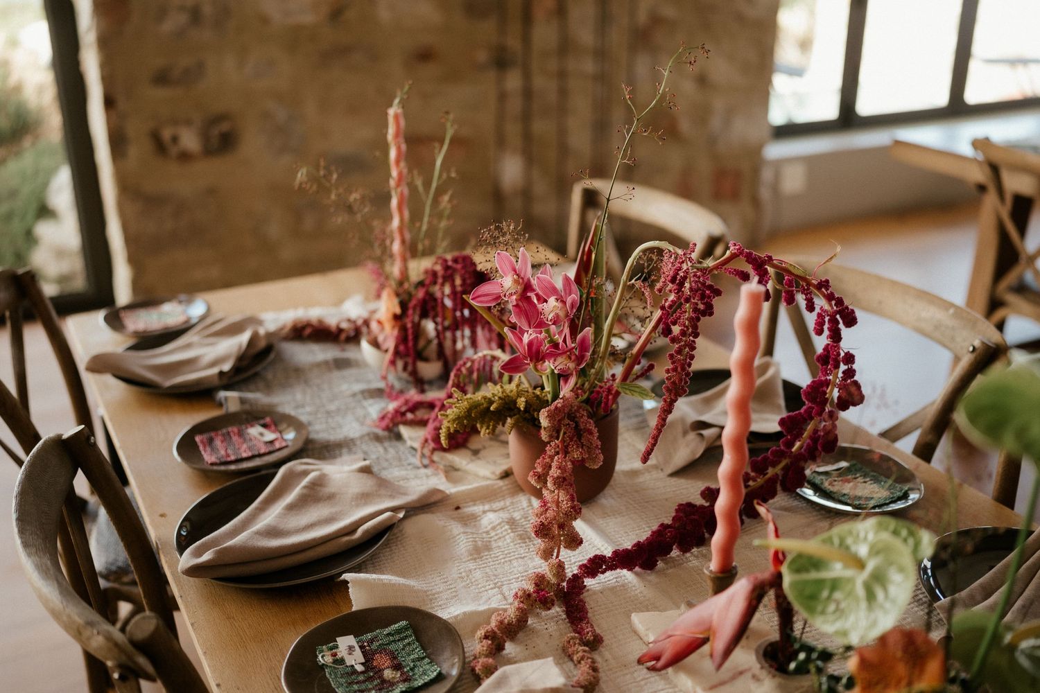 Autumn-themed table setting with burgundy floral arrangements and place settings on a wooden farmhouse table.