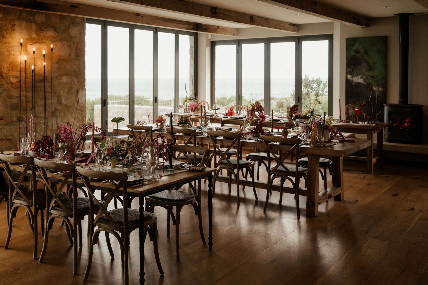Elegant dining room setup with rustic wooden tables, cross-back chairs and large windows overlooking scenic views.
