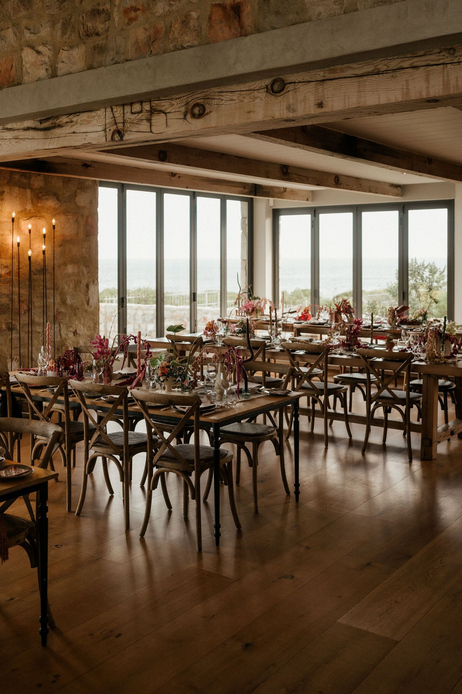 Rustic wedding reception venue with large windows, wooden tables and stunning countryside views.