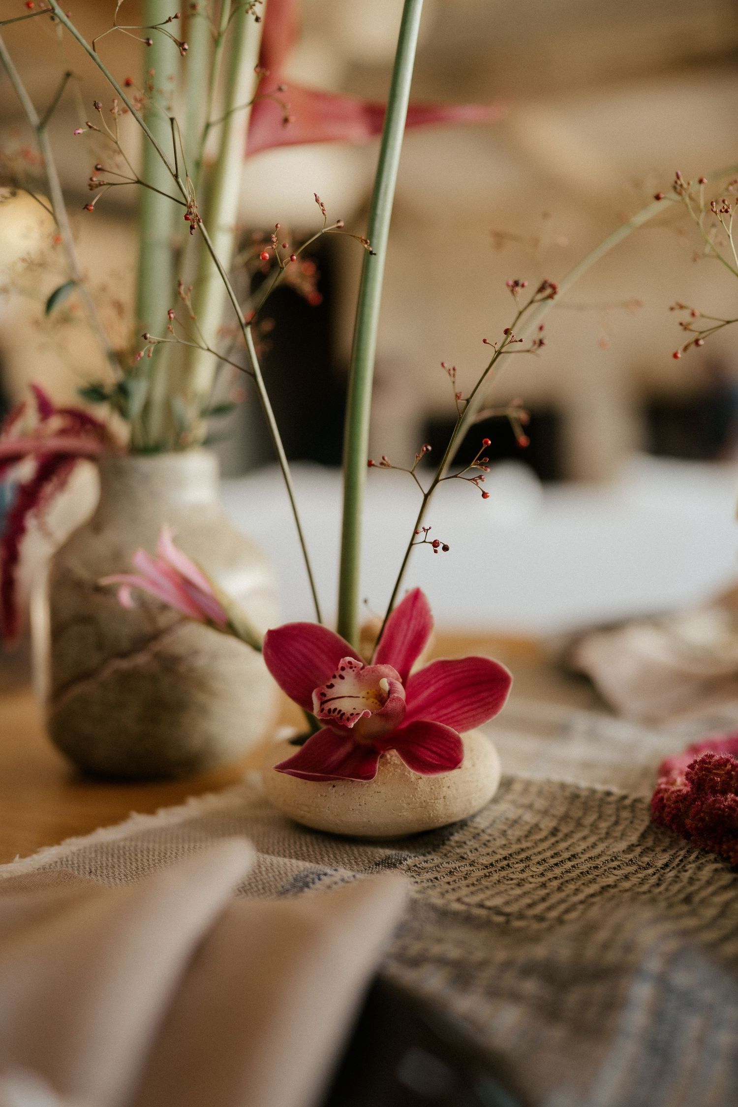 Delicate red orchid flower arrangement with natural elements on burlap table setting.