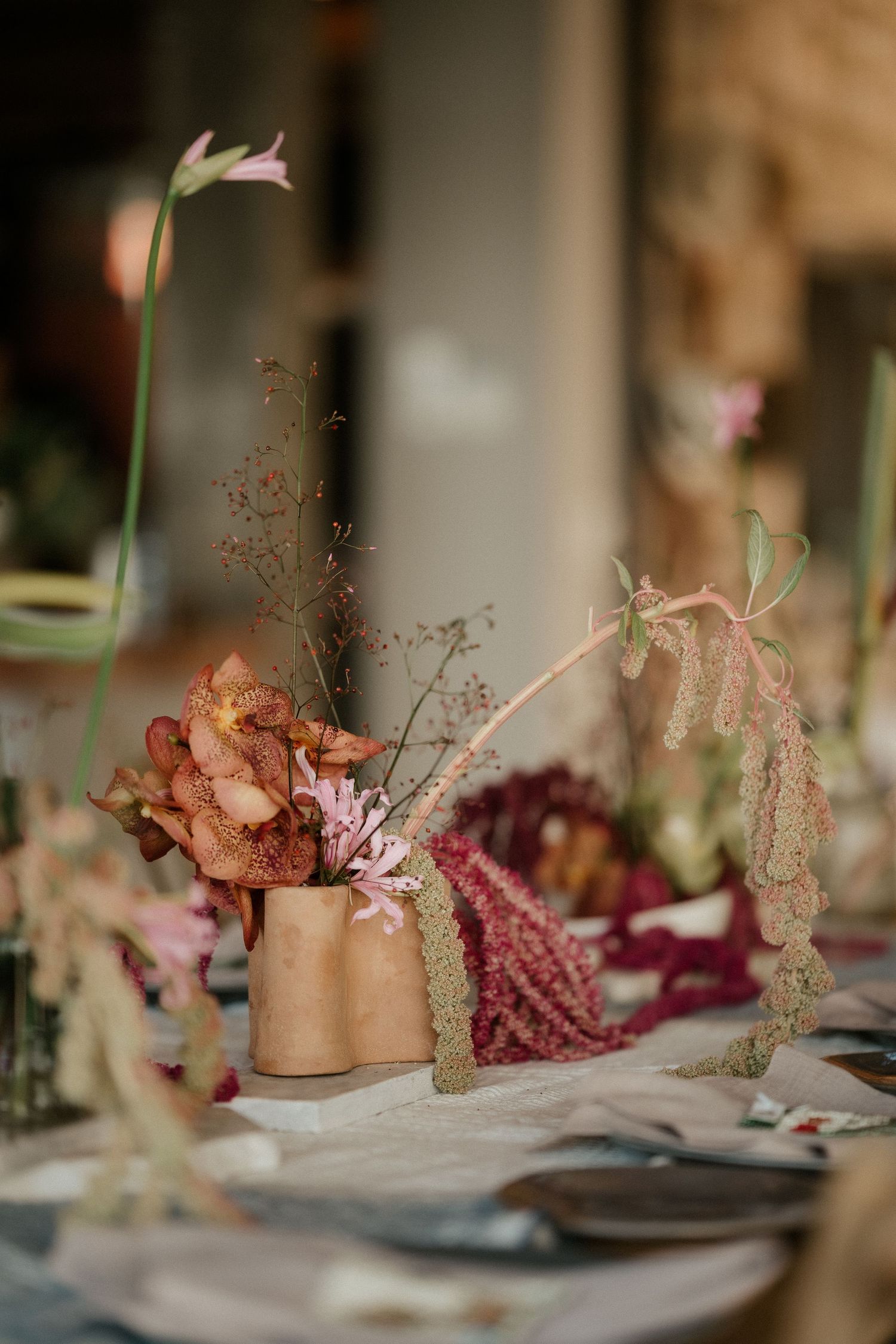 Delicate floral centerpiece with dried flowers and stems in earthy copper-toned vases.