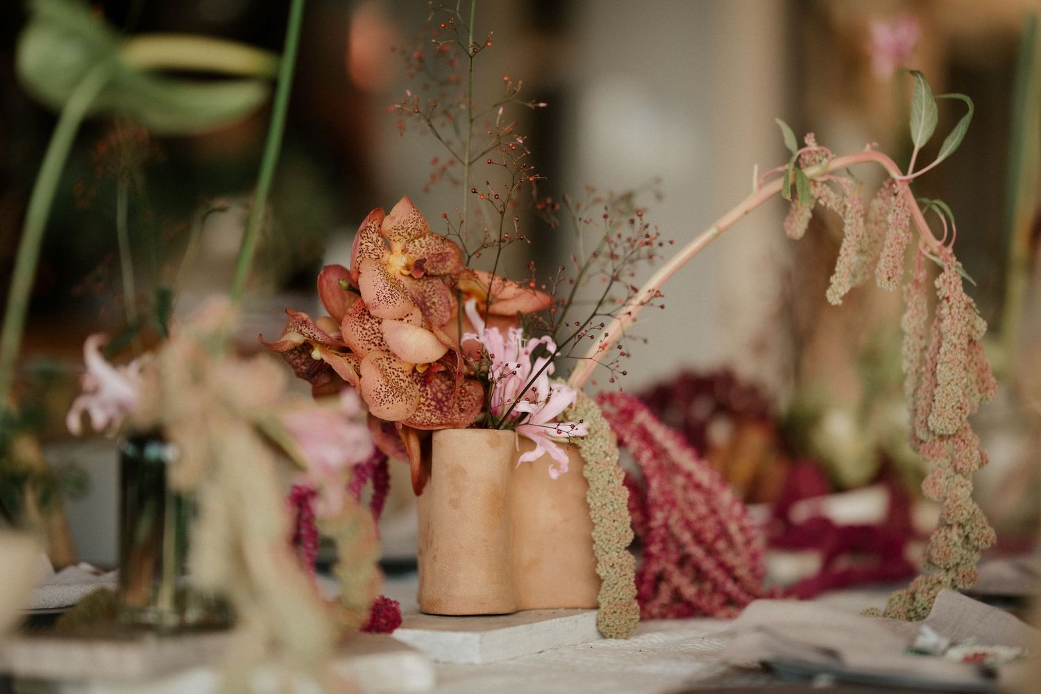Dried floral arrangement in a copper vase with delicate stems and petals at a wedding table setting.