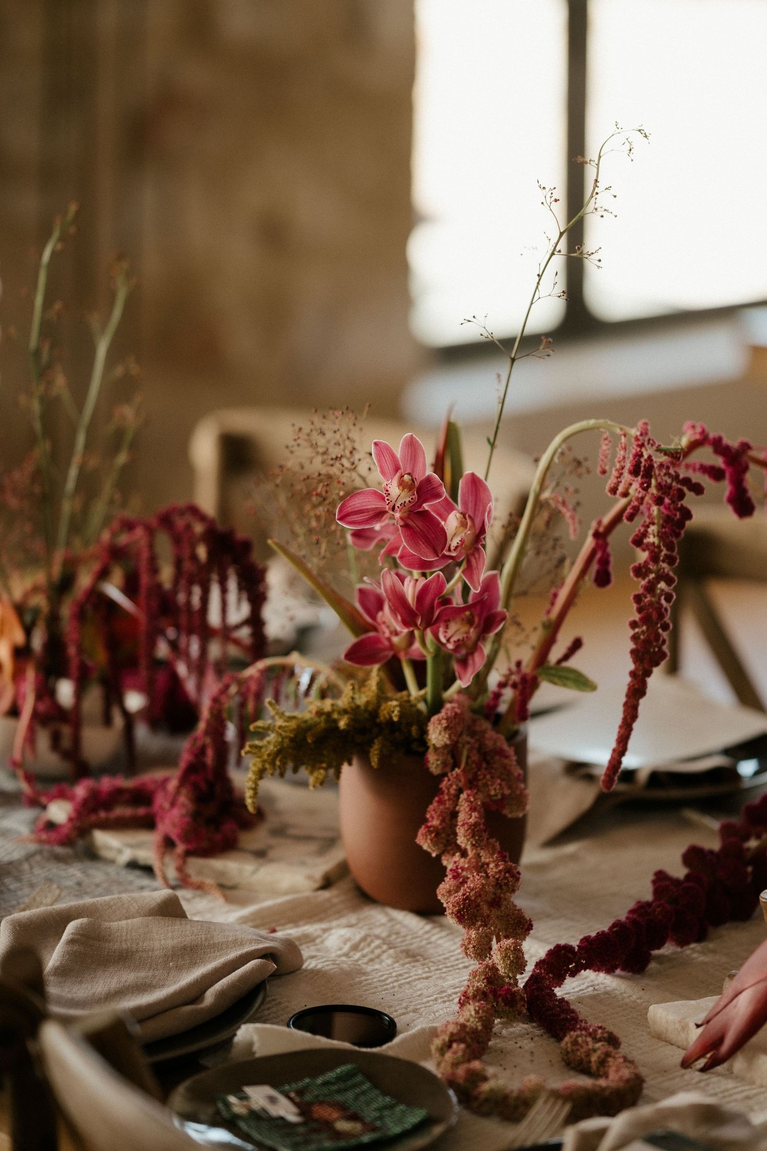 Pink flowers and dried botanical arrangements on a table with place settings.