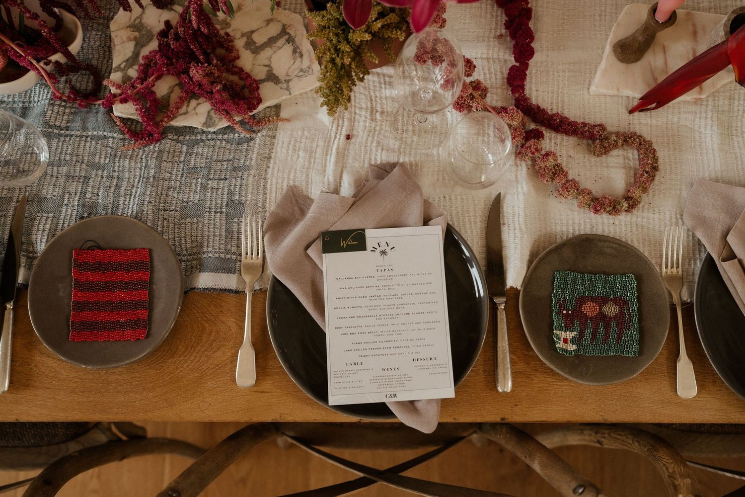Wedding table place settings with menus and decorative floral garlands on a wooden surface.
