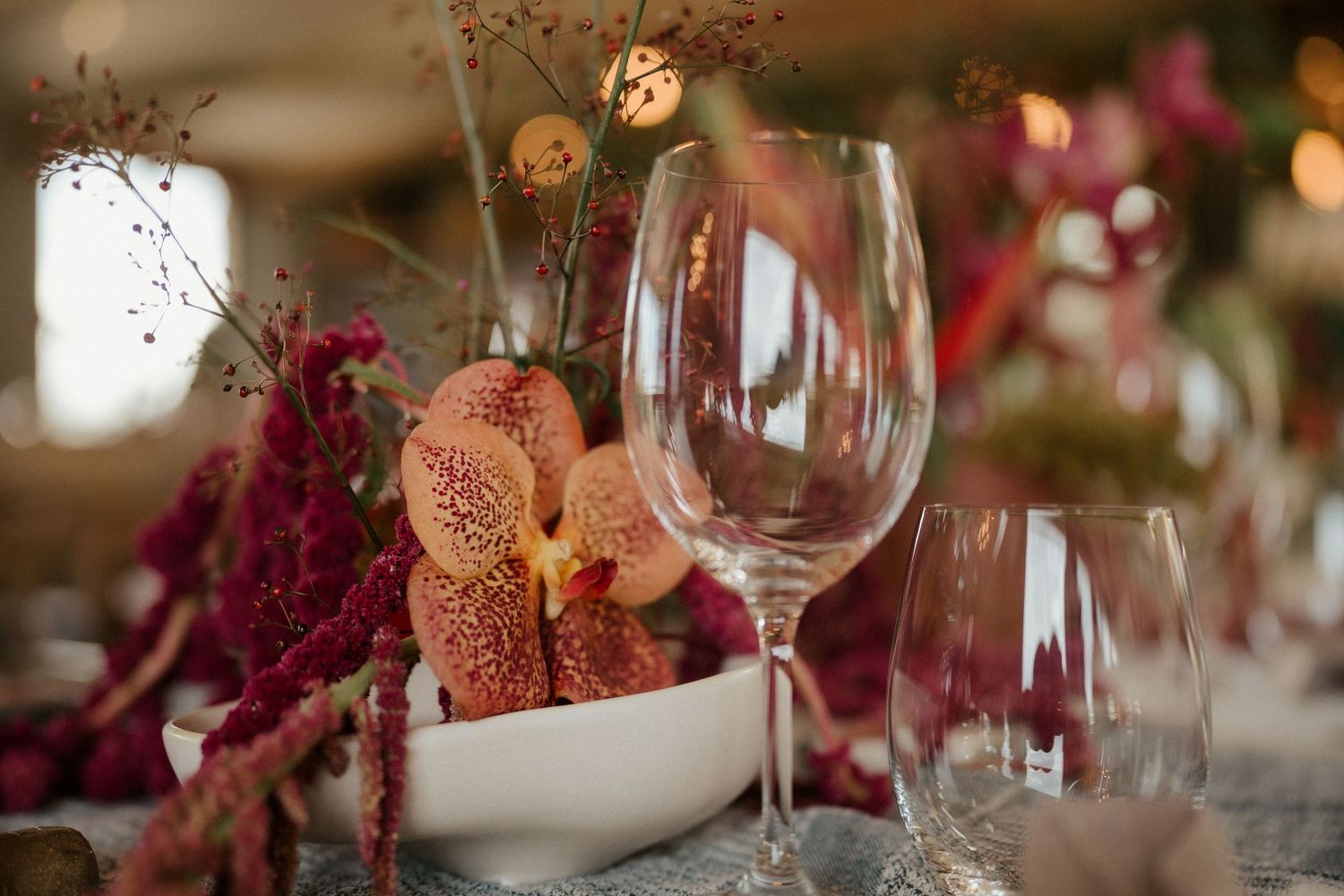 Close-up of wine glasses and pink floral centerpieces on an elegantly set dining table.