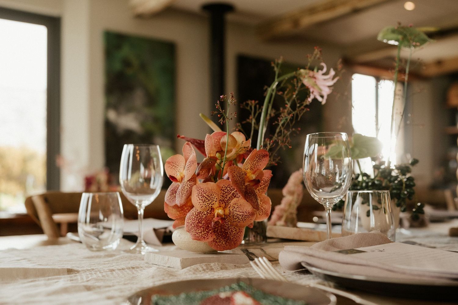 Elegant table setting with coral floral centerpiece, wine glasses and place settings in warm natural lighting.