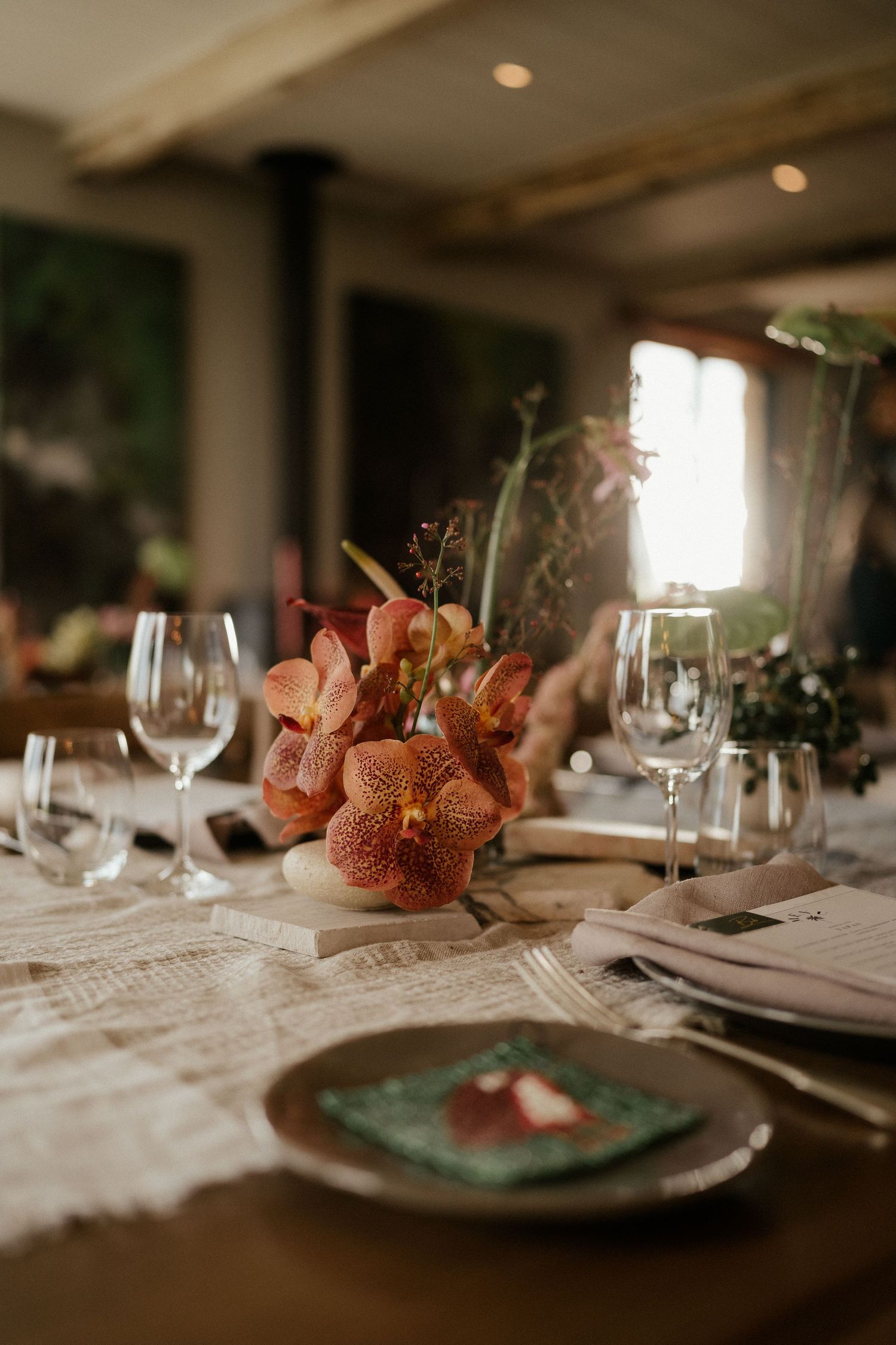 Romantic table setting with coral-colored orchid centerpiece and wine glasses on linen tablecloth.