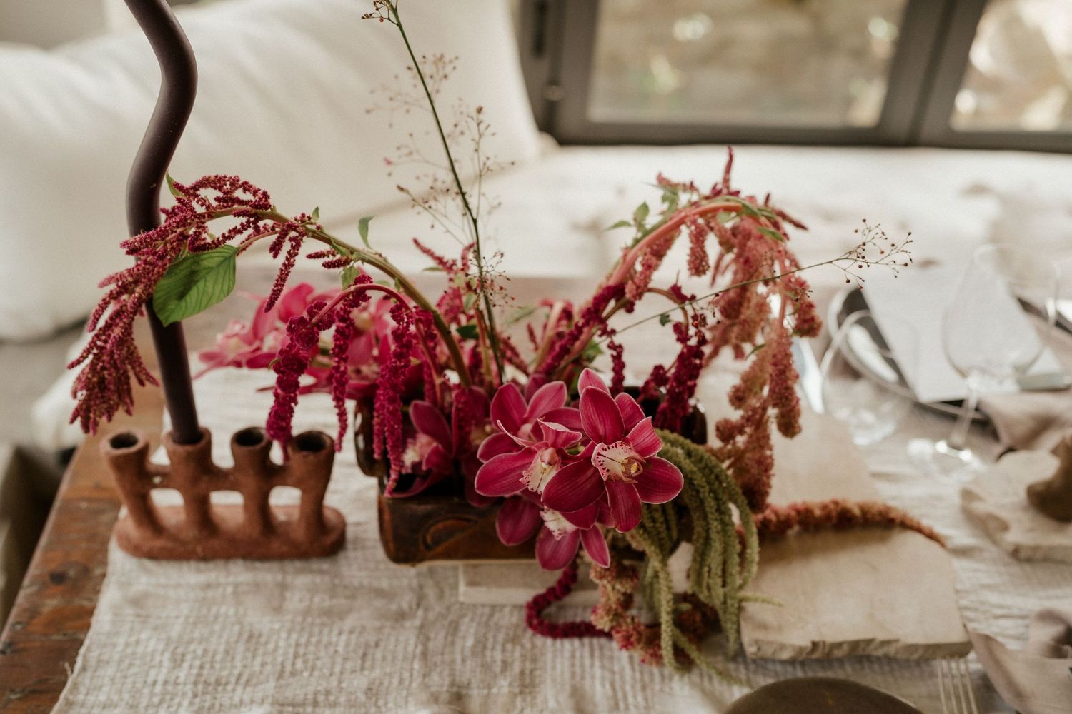 Red floral arrangements in wooden vessels on a rustic table with delicate dried flowers and natural elements.