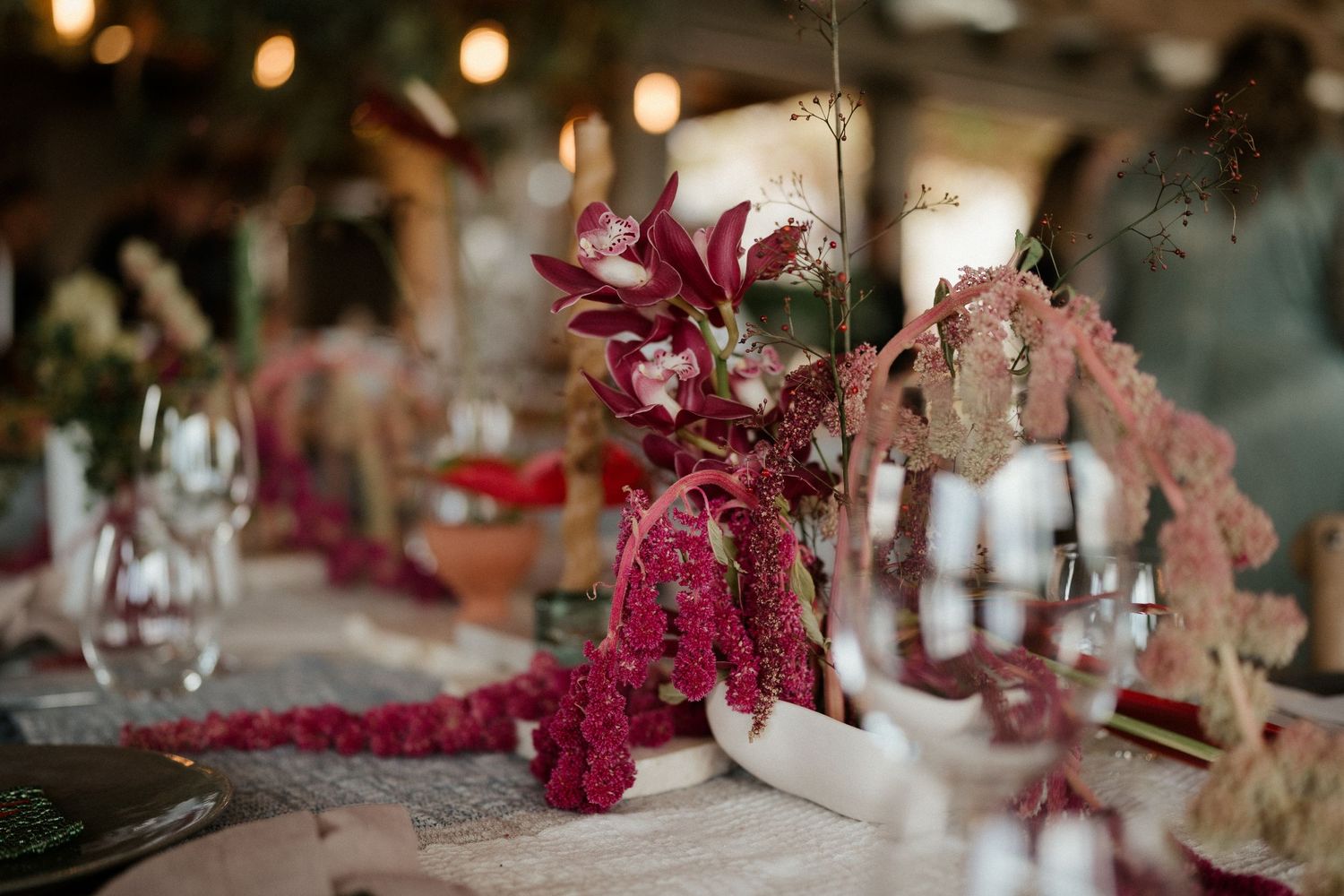 An elegant table setting features deep pink floral centerpieces and glowing candles for a wedding reception.