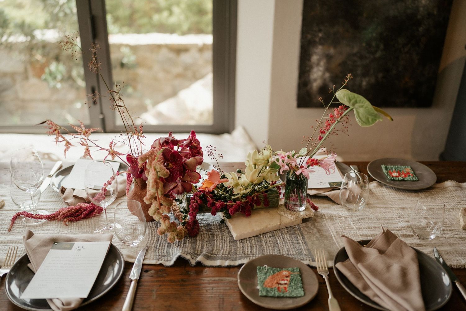 Elegant tablescape with deep red floral centerpiece and place settings on wooden dining table near window.