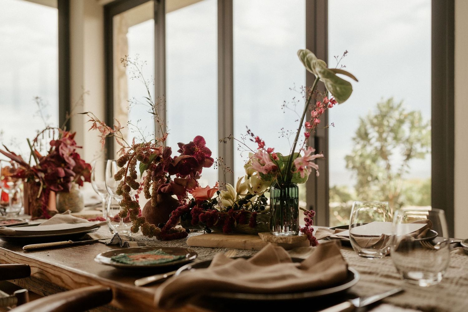 Elegant autumn wedding tablescape with dried red floral arrangements and rustic place settings in a sunlit room.