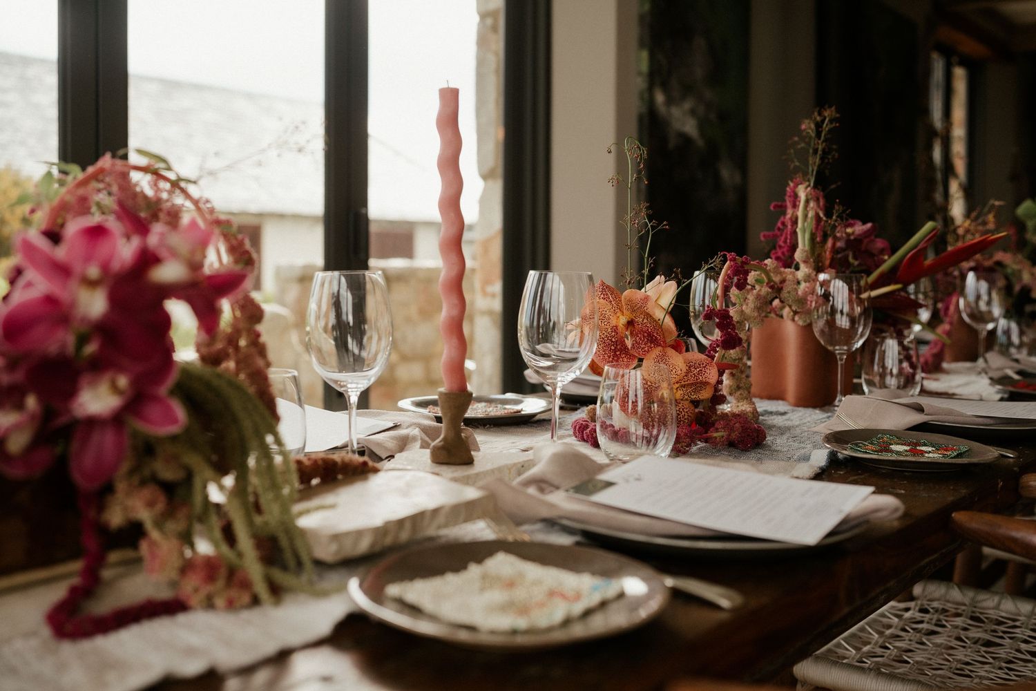 Elegant table setting with wine glasses, pink floral arrangements and candlelight for a special occasion.