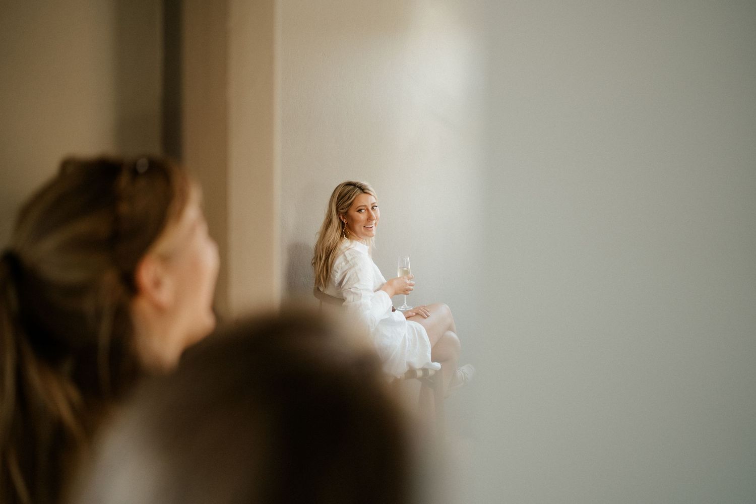 Someone in white sits in a sun-lit room while others look on in soft focus in the foreground.
