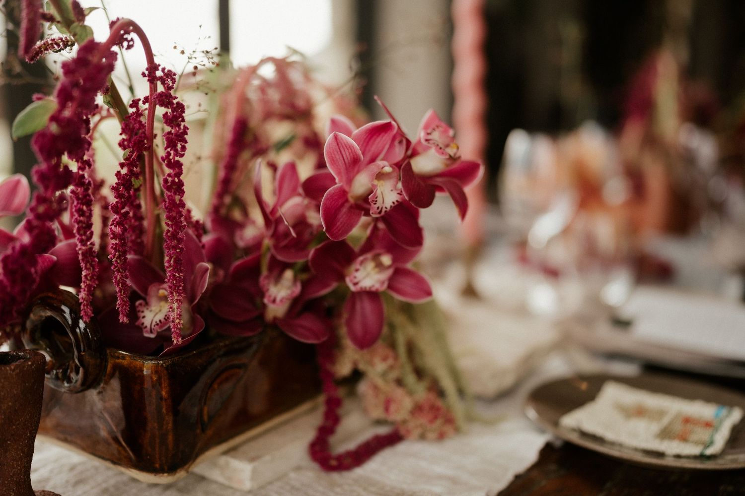 Pink and burgundy floral centerpiece with orchids on an elegant table setting.