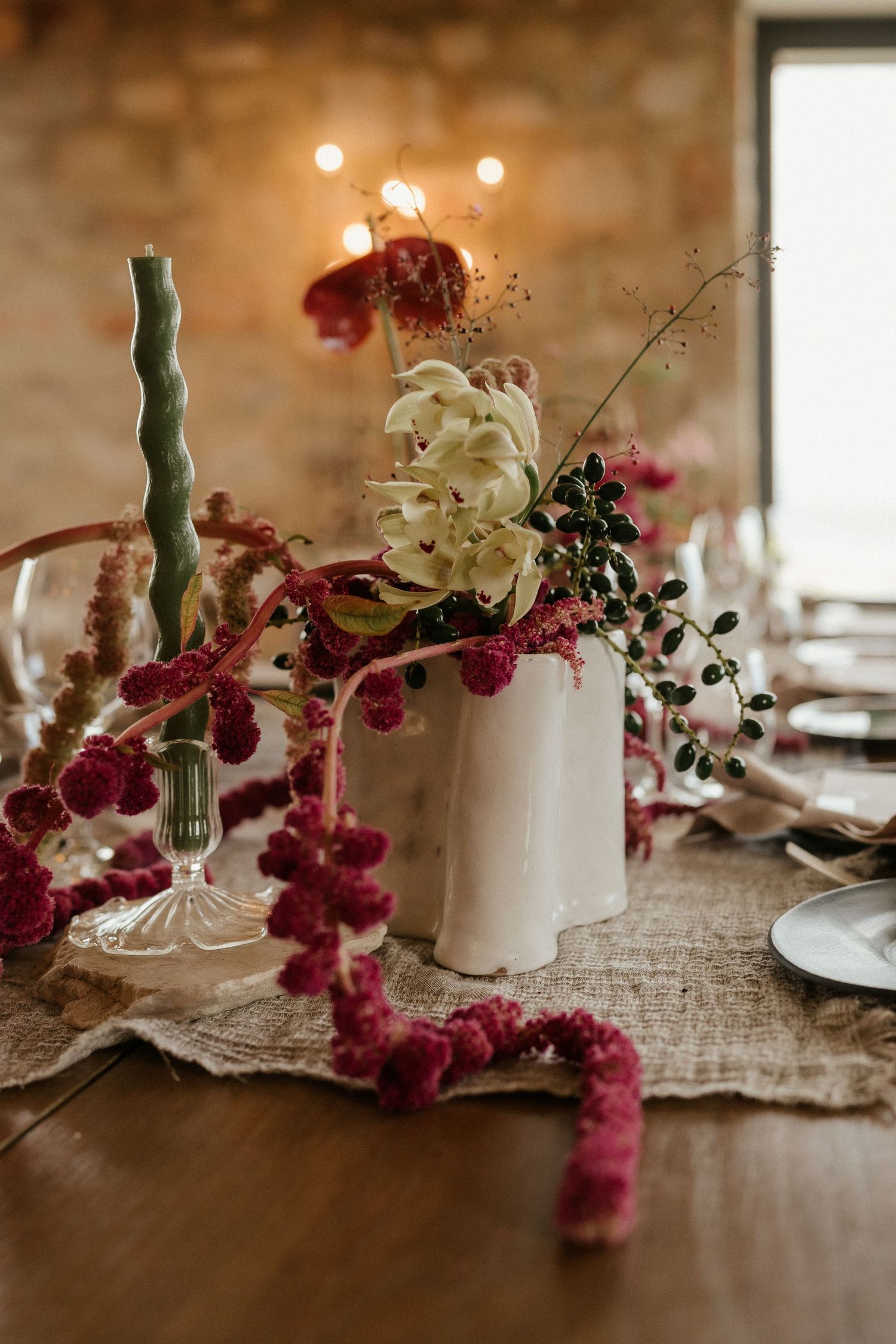 Artistic floral arrangement with white and burgundy flowers in a ceramic vase on linen tablecloth.