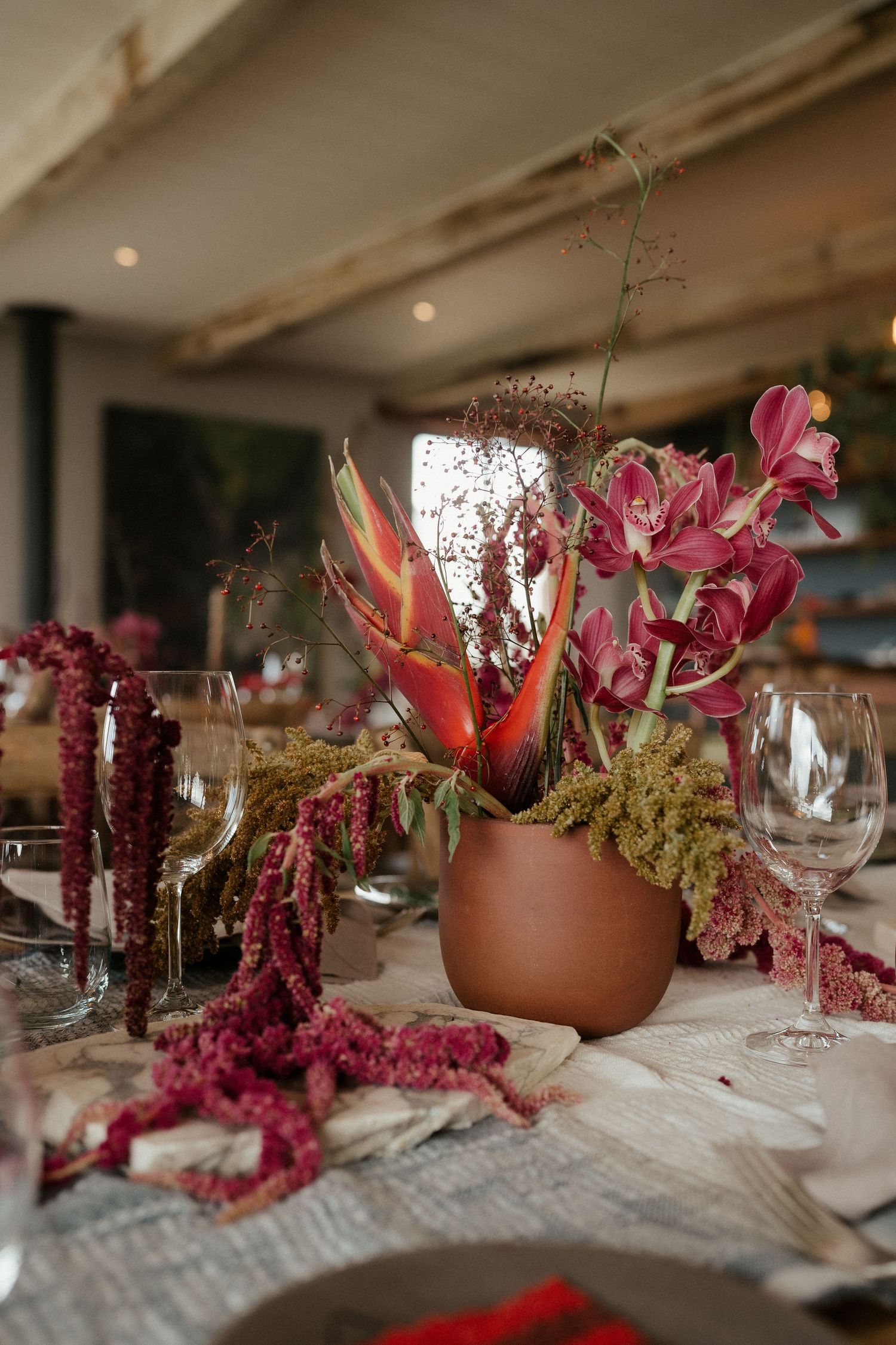 Tropical and burgundy floral centerpiece in terra cotta pot with trailing amaranthus.