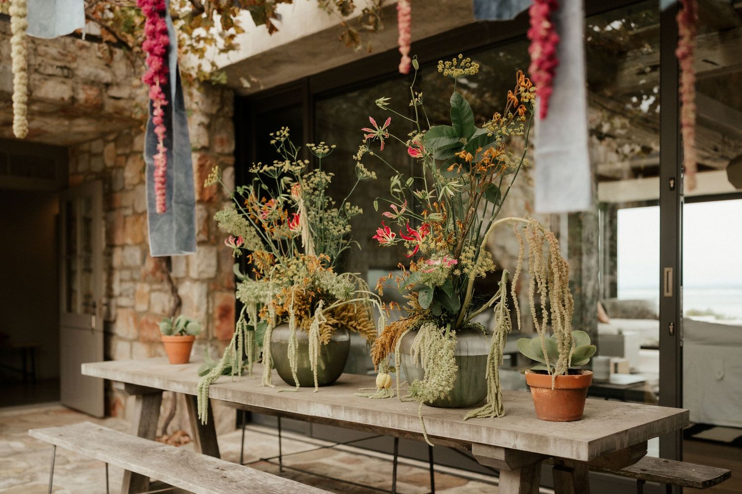 Rustic wooden bench with potted plants and hanging pink decorations in a greenhouse-like setting.