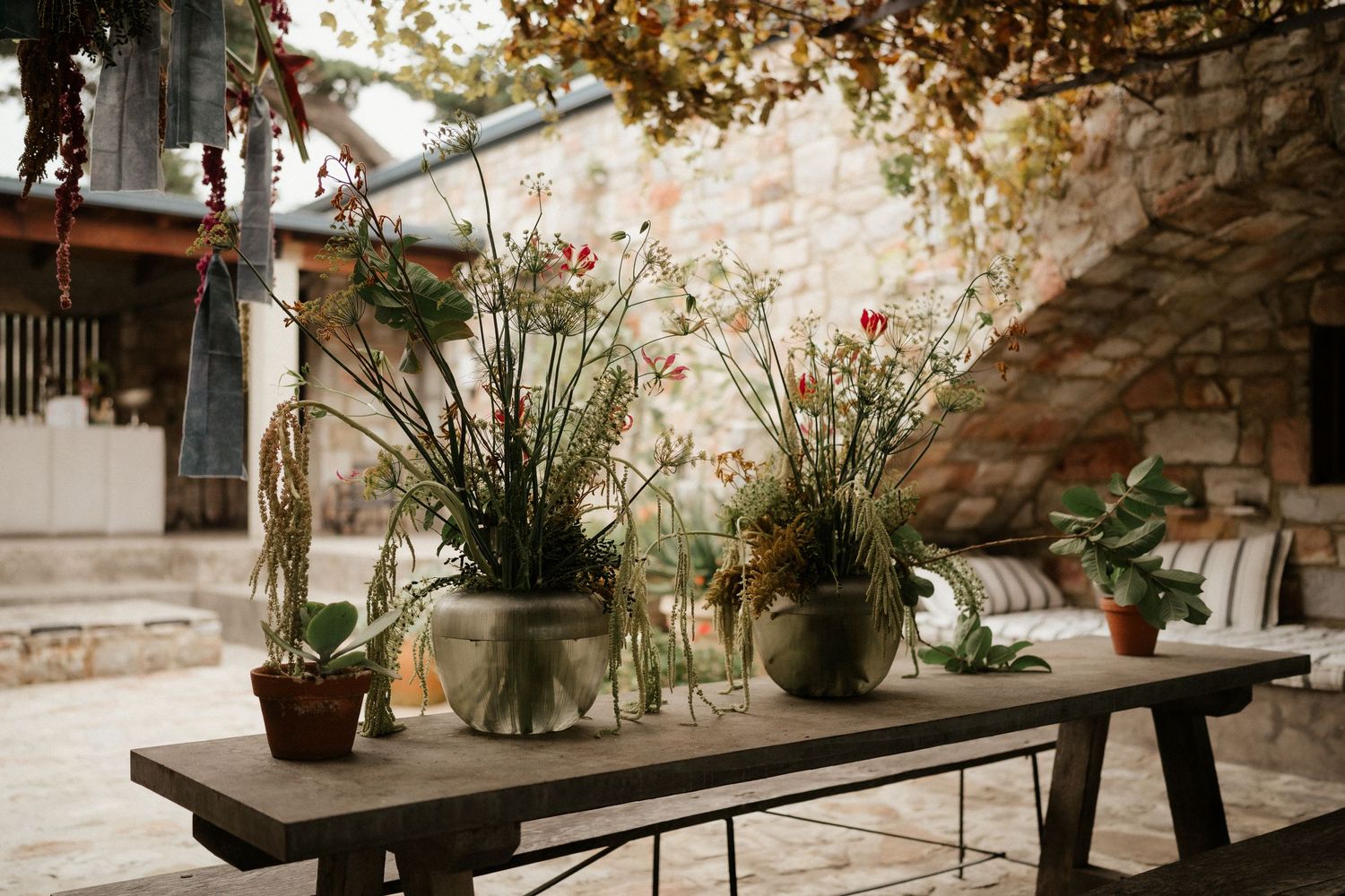 Rustic outdoor table setting with potted plants and flowers in a garden patio area.