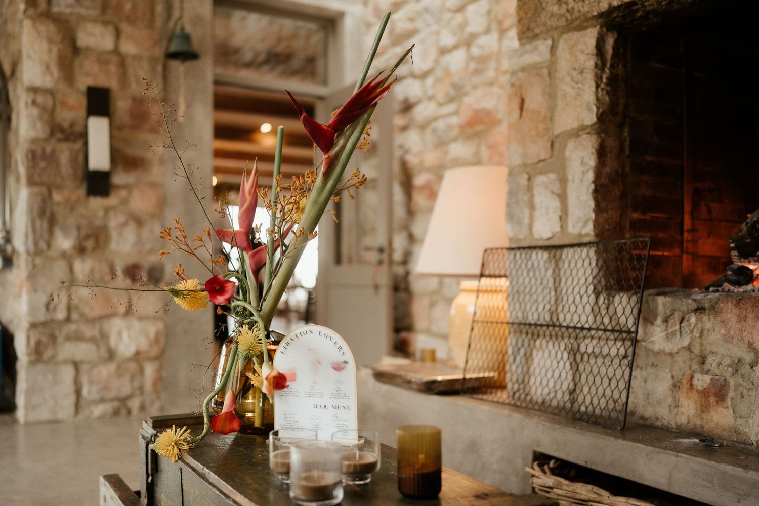 Colorful floral arrangement with red blooms displayed against rustic stone wall interior.