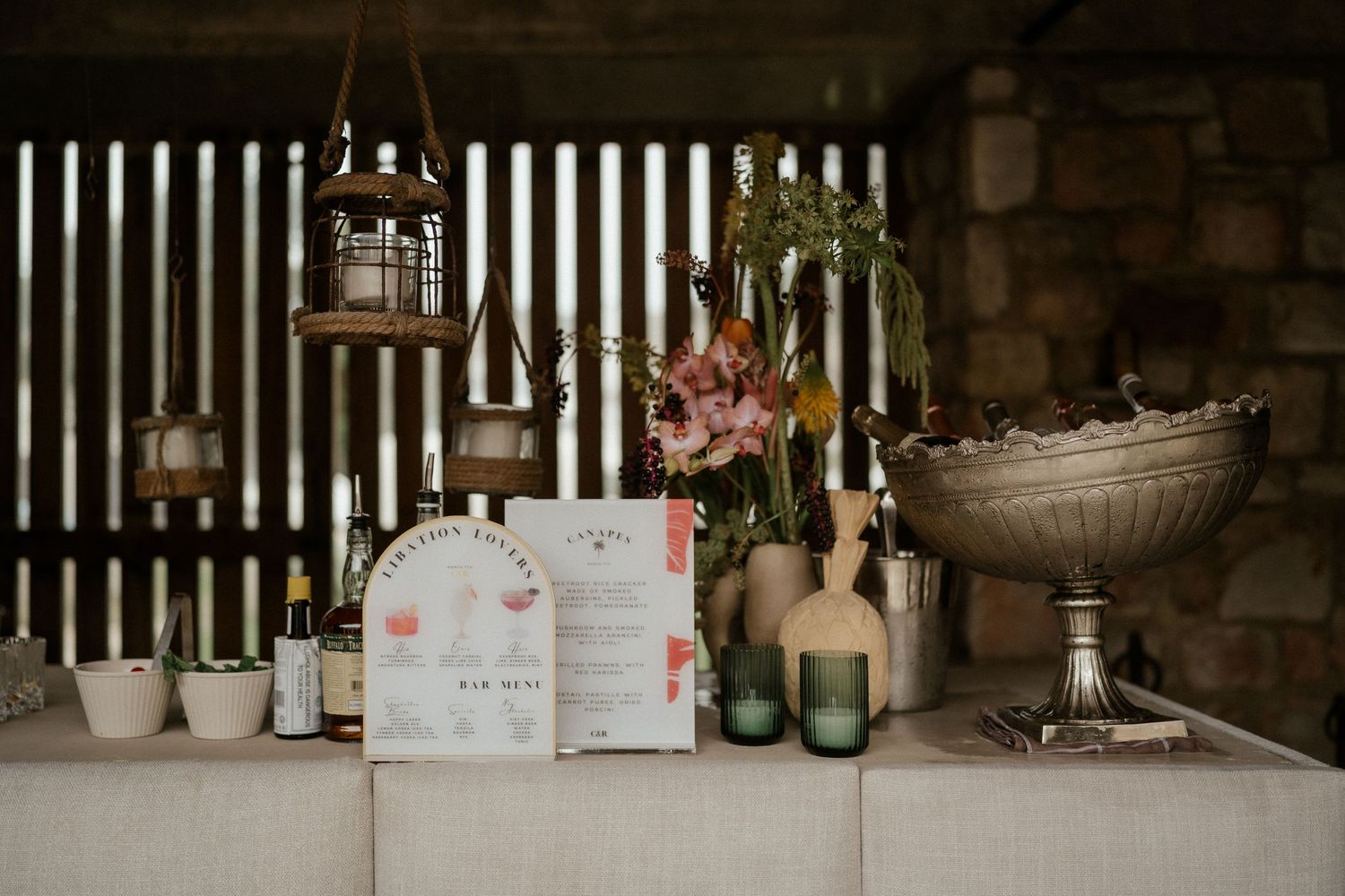 Vintage wedding decor with lanterns, flowers and drinks displayed on a white counter against wooden slats.