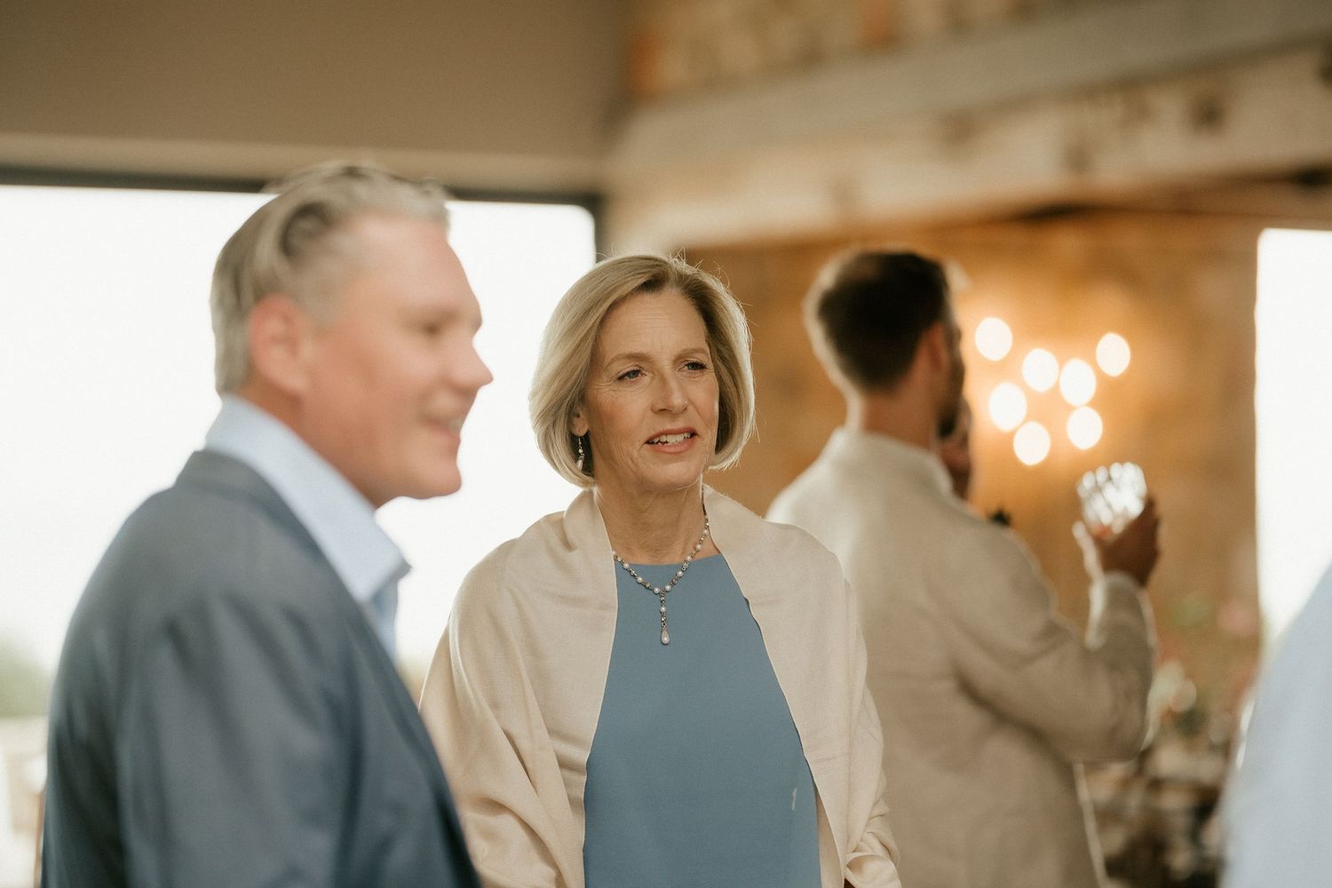 People engaged in conversation at an indoor event with warm lighting and blurred background decorations.