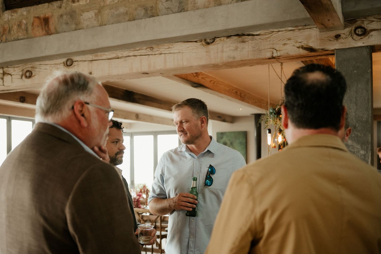 Three men engaged in conversation in a rustic indoor setting with wooden beams.