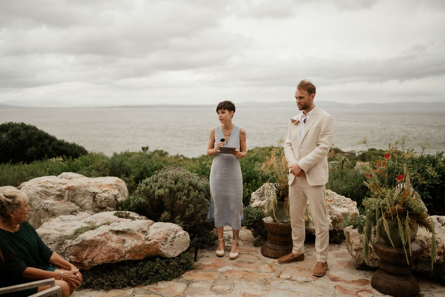 Wedding ceremony guests gather on a coastal stone patio overlooking the ocean.