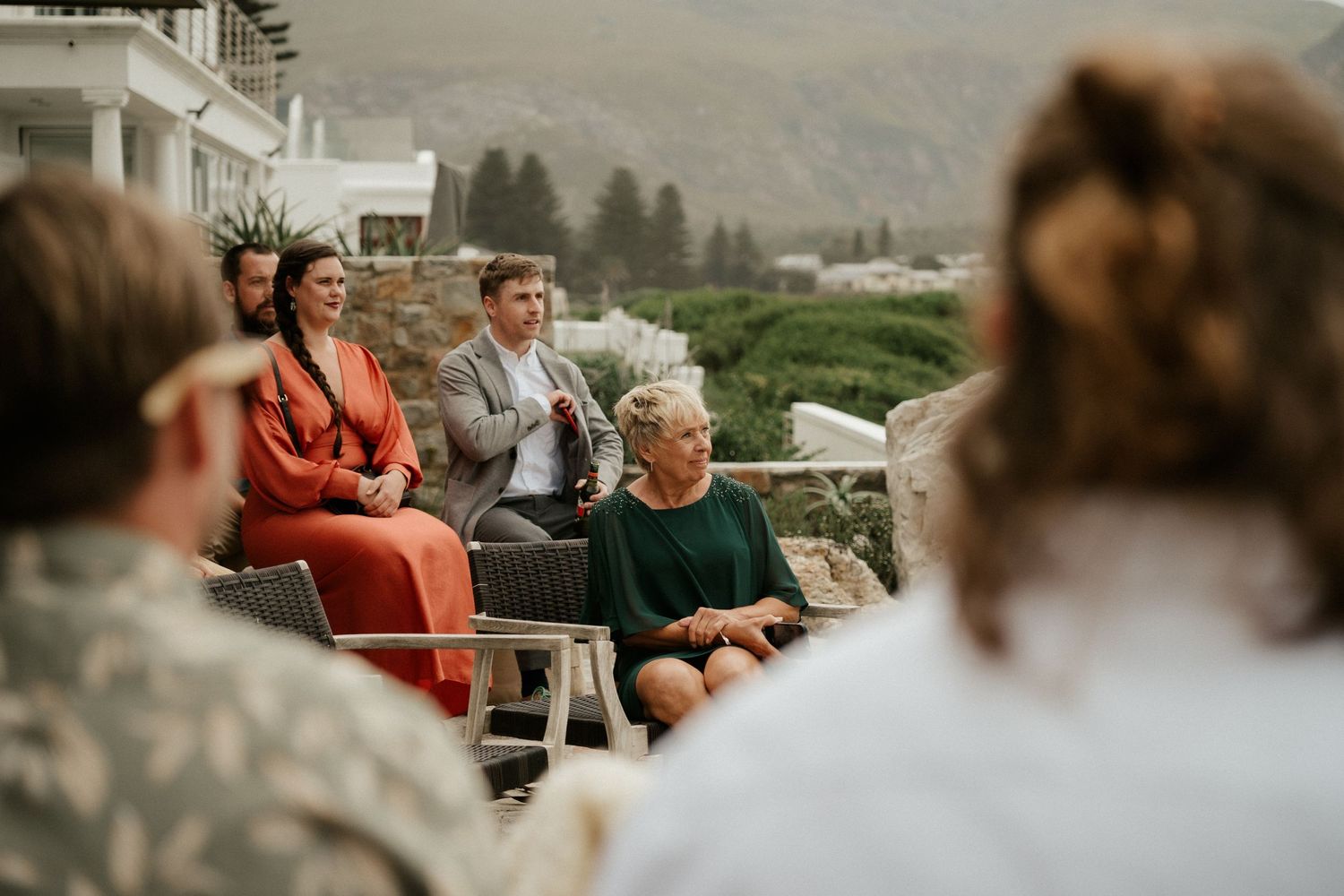 A small outdoor gathering with people seated on chairs against a misty mountain backdrop.