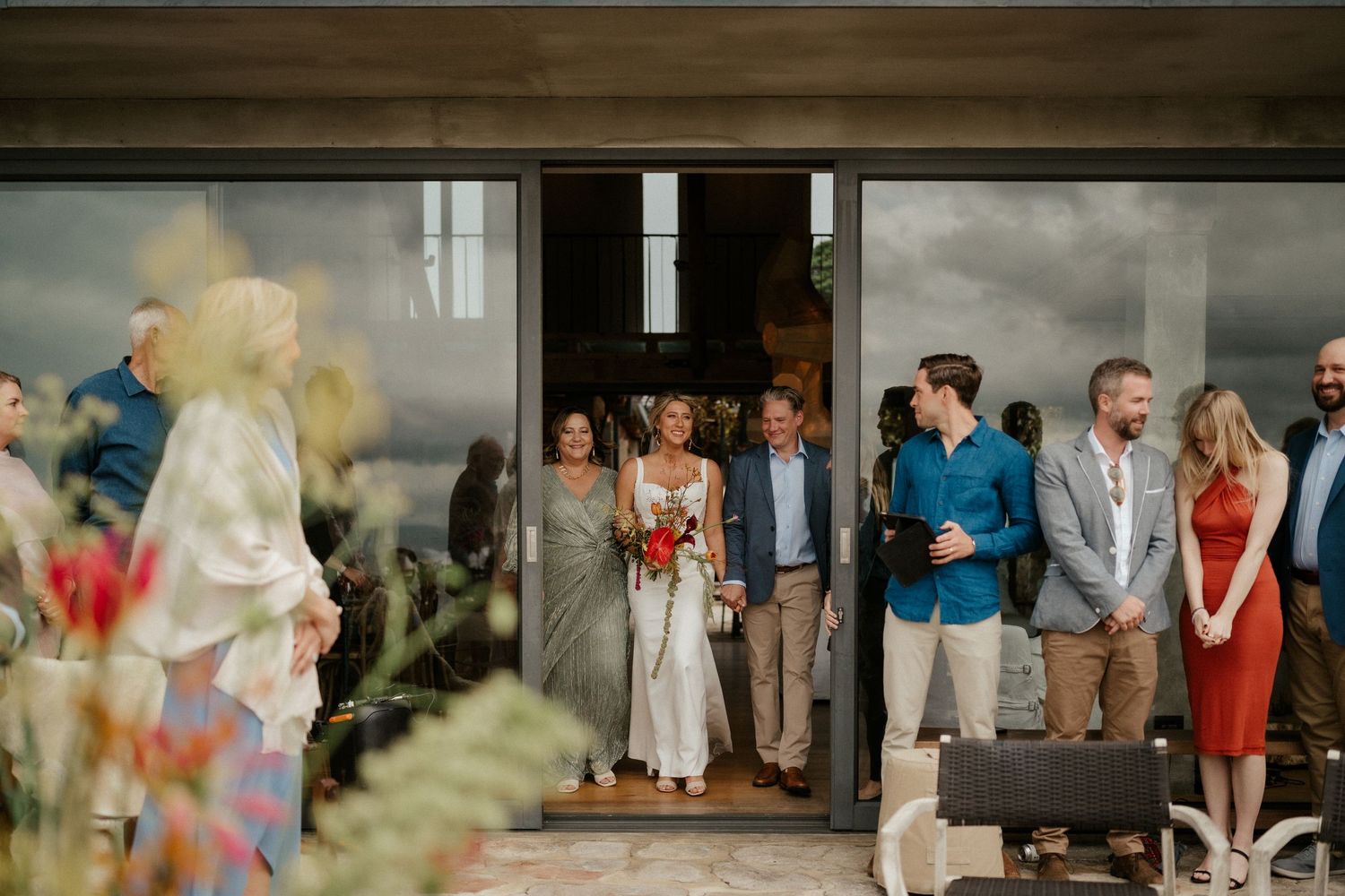 Wedding guests gather under an overhang during an outdoor celebration.