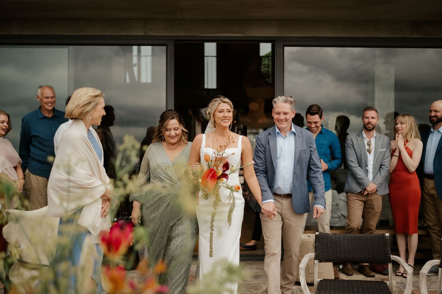 Wedding party and guests gathered outside on a cloudy day for celebration.