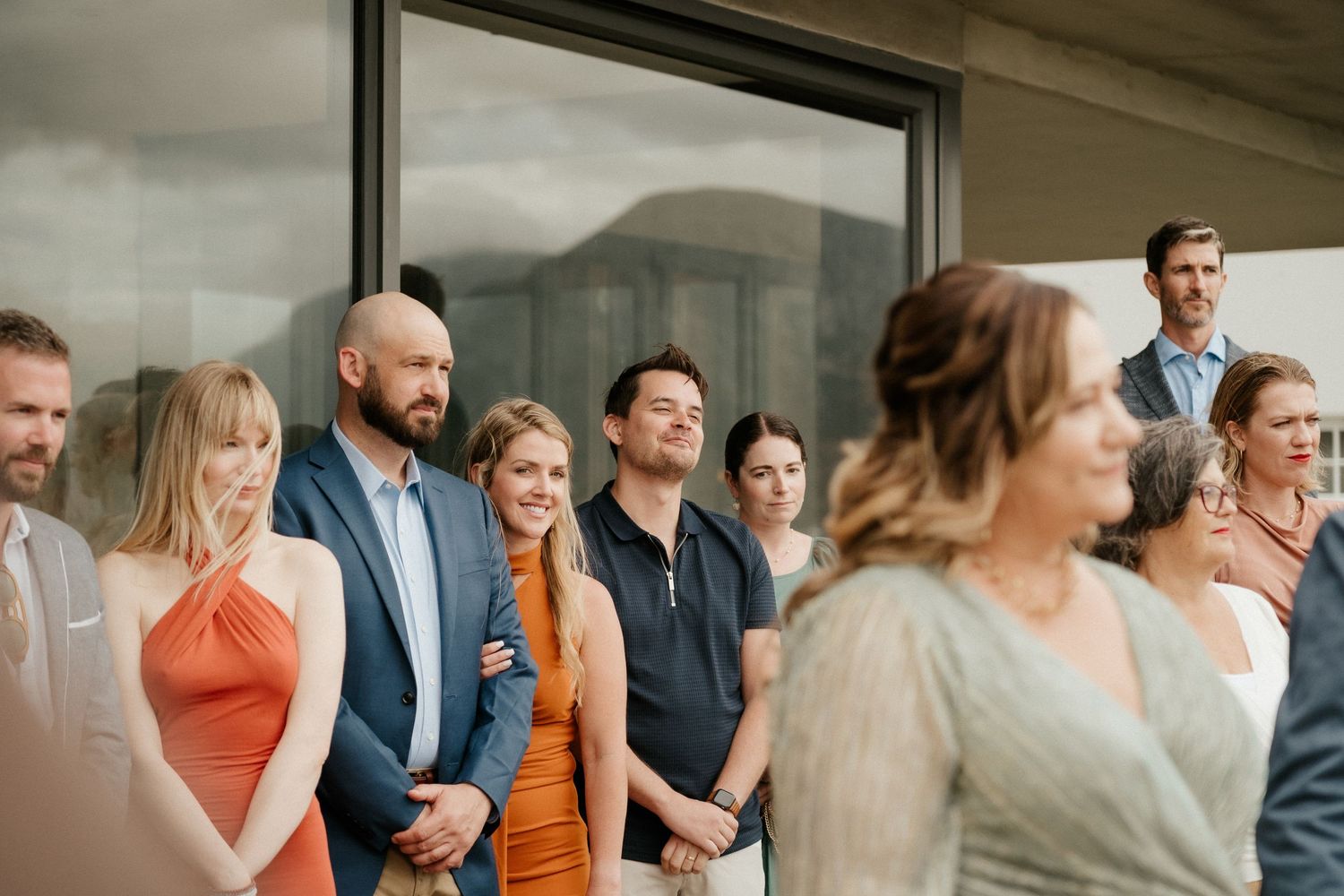 Wedding attendees gather near large glass windows during a celebration.