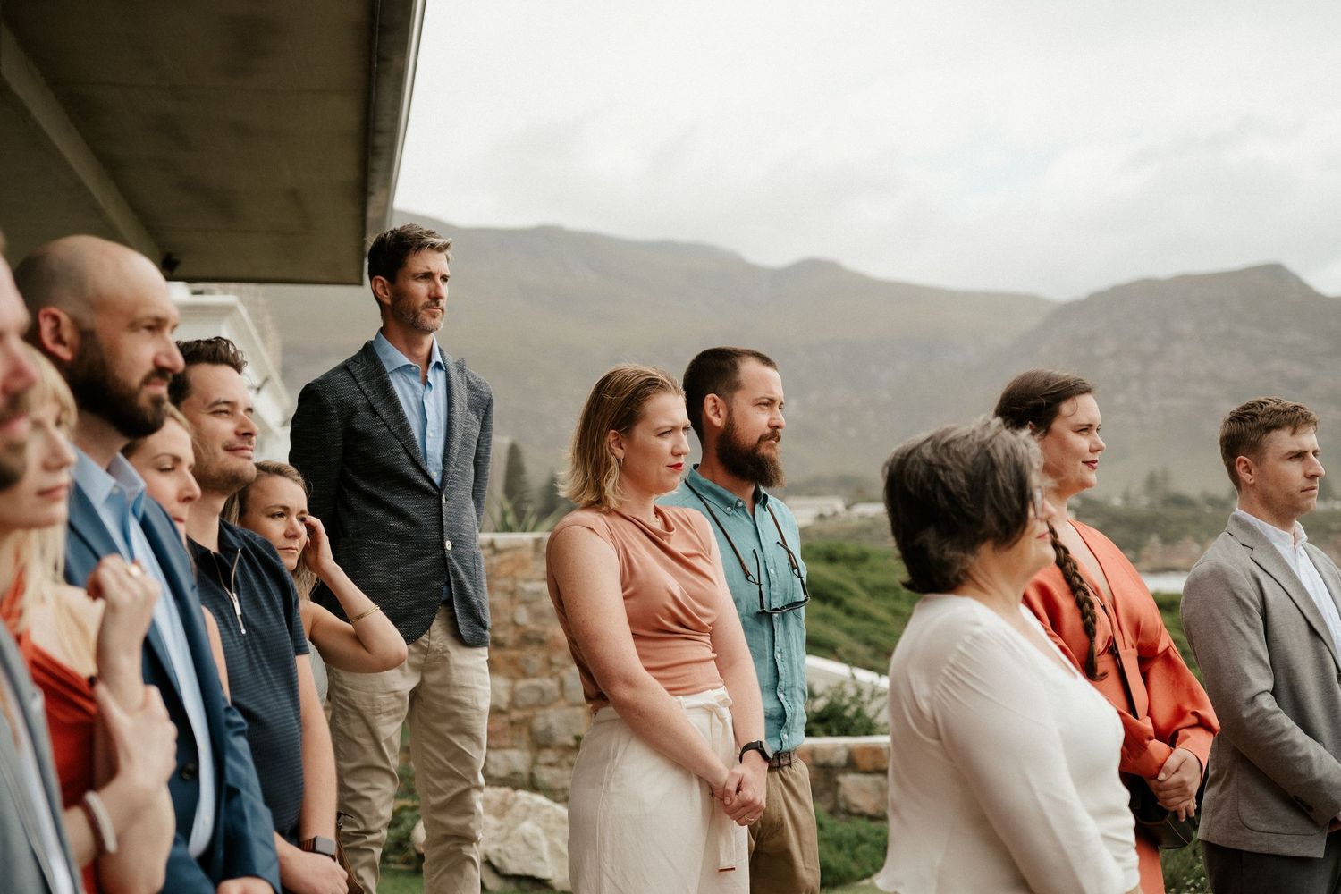 Wedding party members gather outdoors with mountains visible in the background.