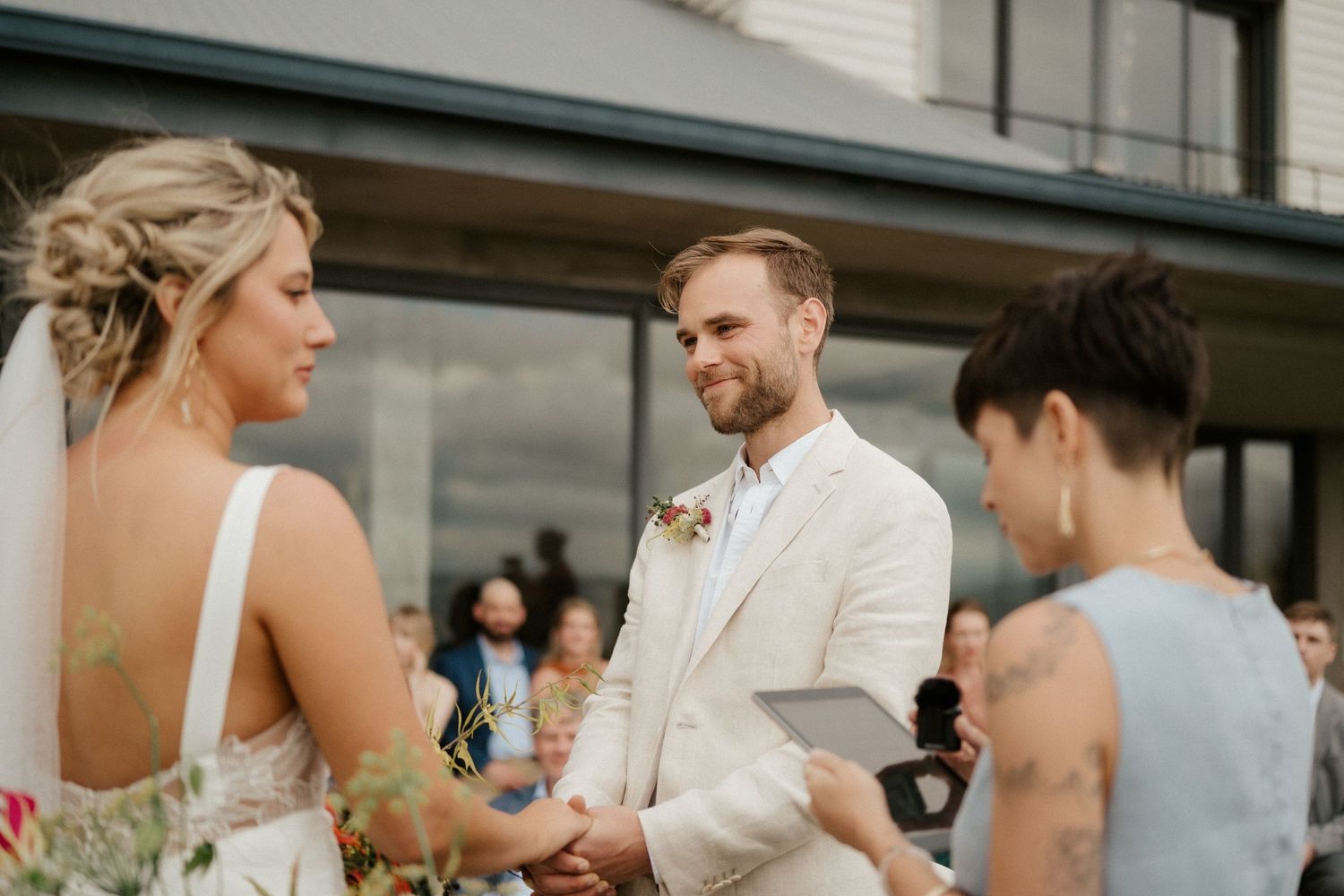 Intimate wedding ceremony moment with couple and officiant in a white suit outdoors.