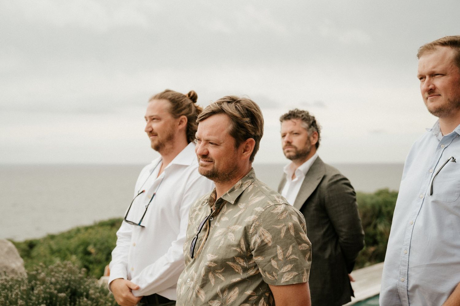 Four people stand together looking out towards the ocean on an overcast day.