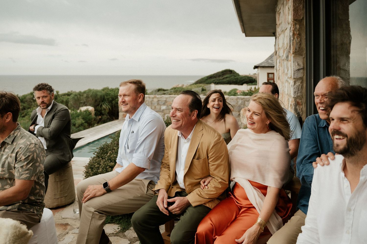 Group gathered casually on outdoor deck with ocean view in background.