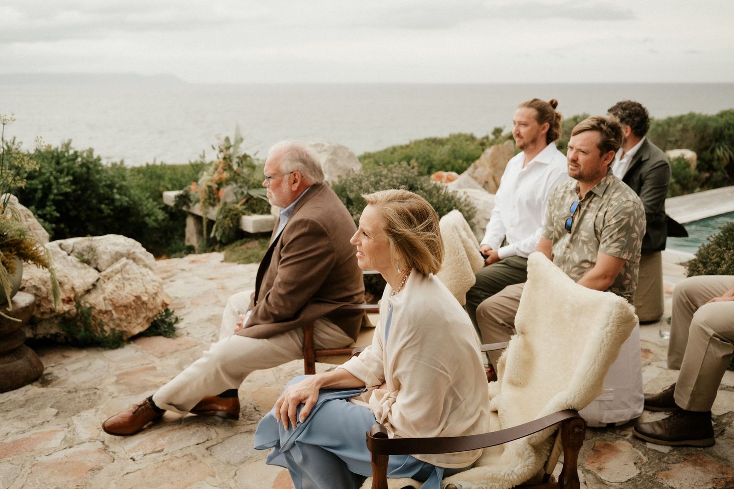 Wedding guests seated on rocks overlooking a scenic mountain vista during outdoor ceremony.