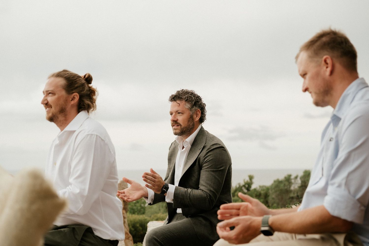 Three people share a moment outdoors against an overcast sky.