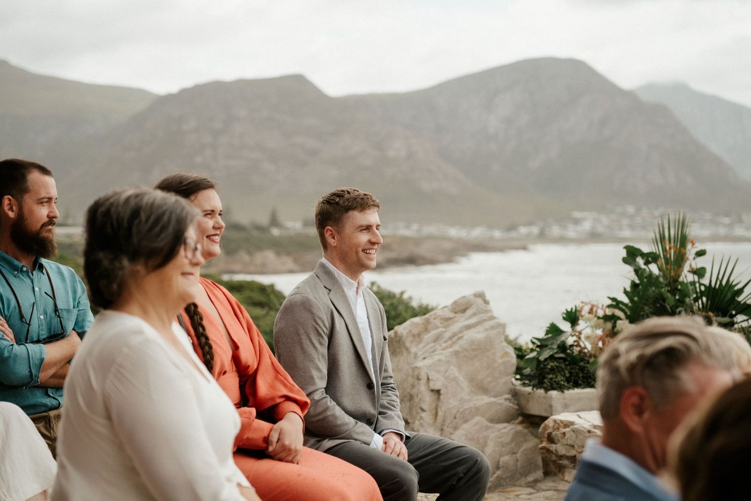 Wedding guests seated on a cliff overlooking a scenic mountain coastline view.