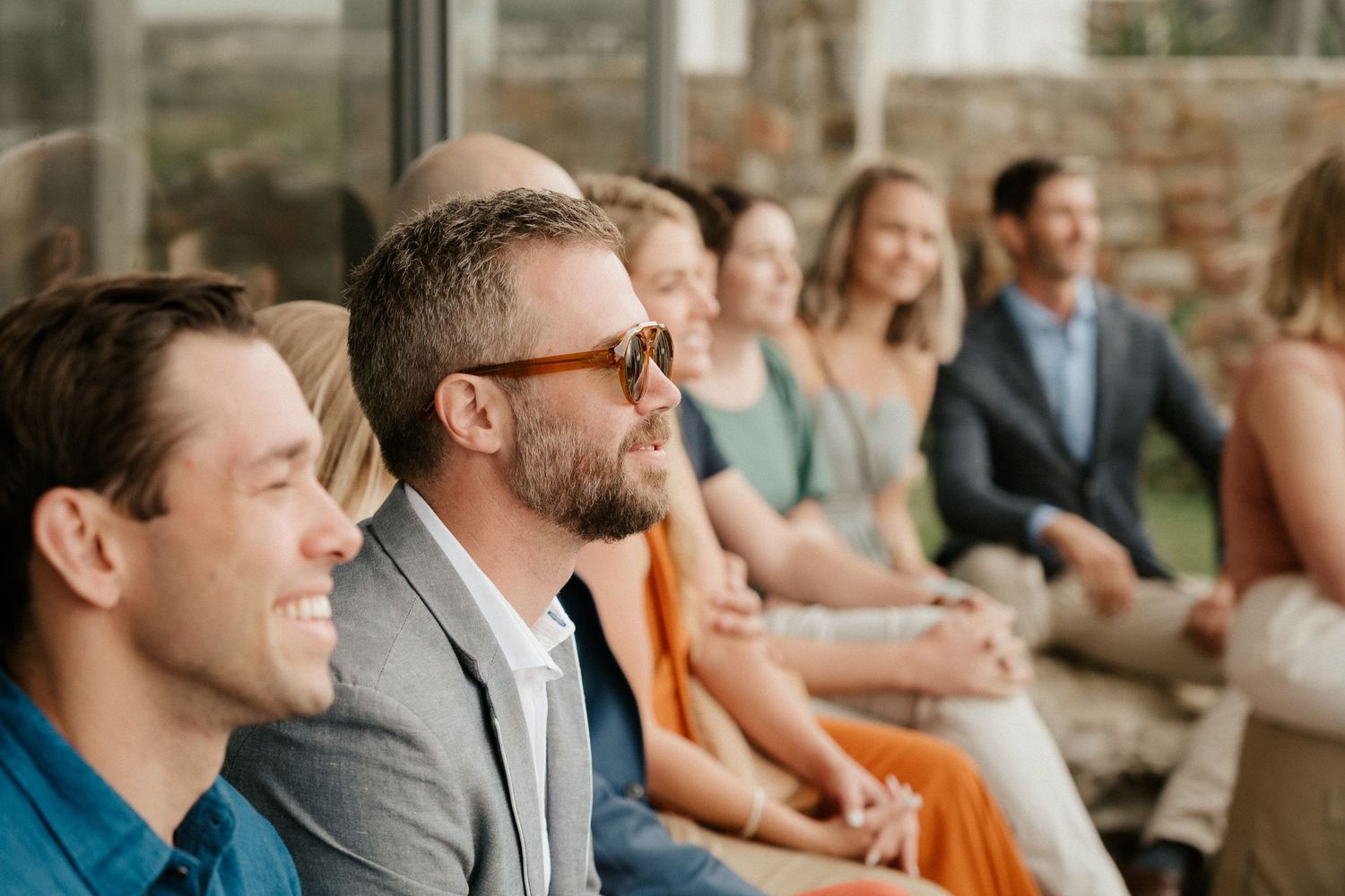 Wedding guests smile and laugh together during an outdoor ceremony gathering.
