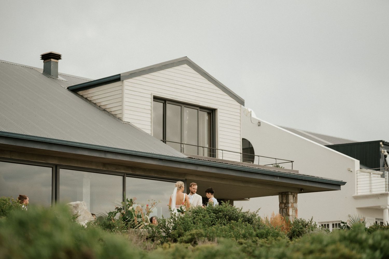 Modern white house with coastal architecture features people enjoying the rooftop garden area.