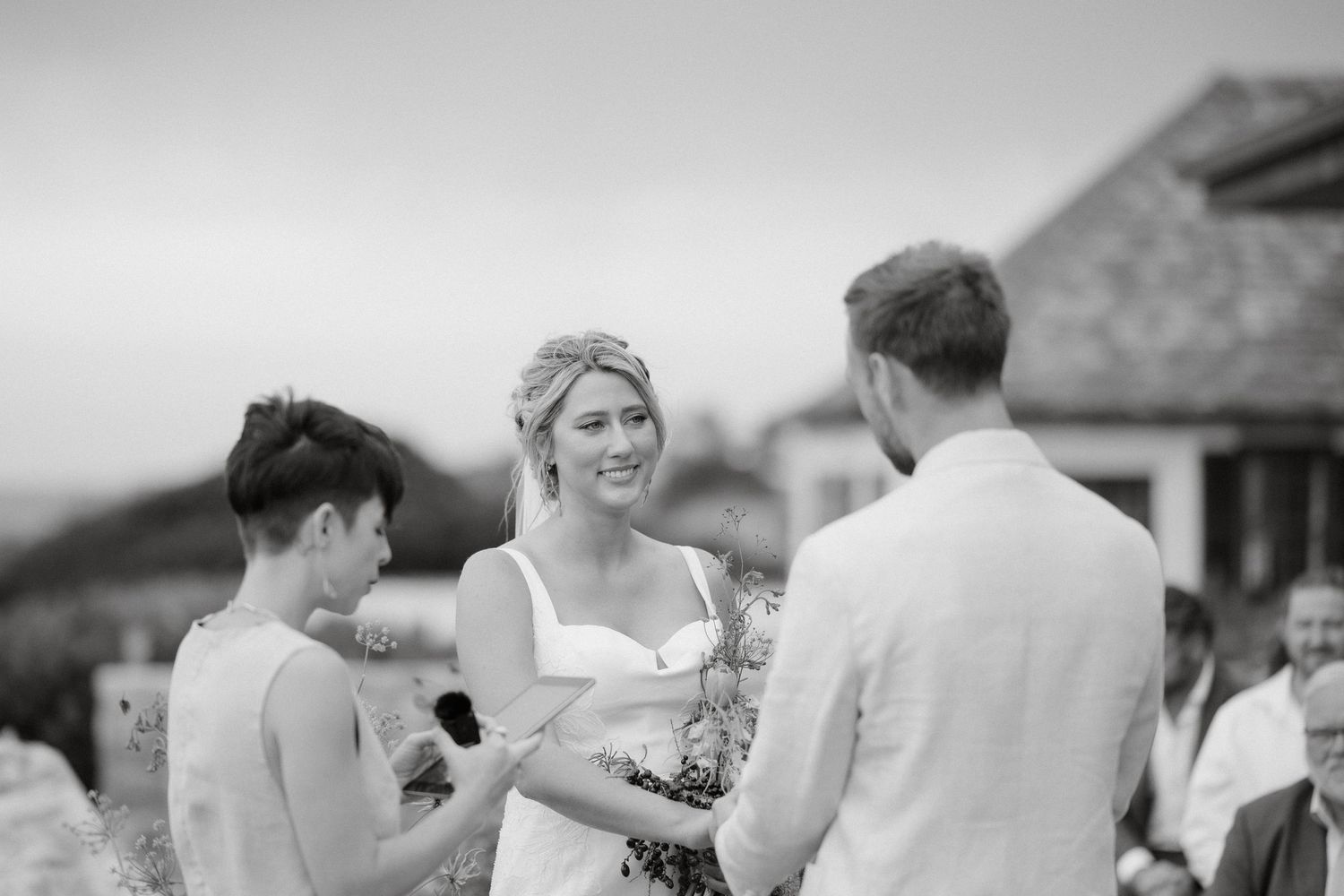 Black and white outdoor wedding ceremony moment with stone buildings in background.