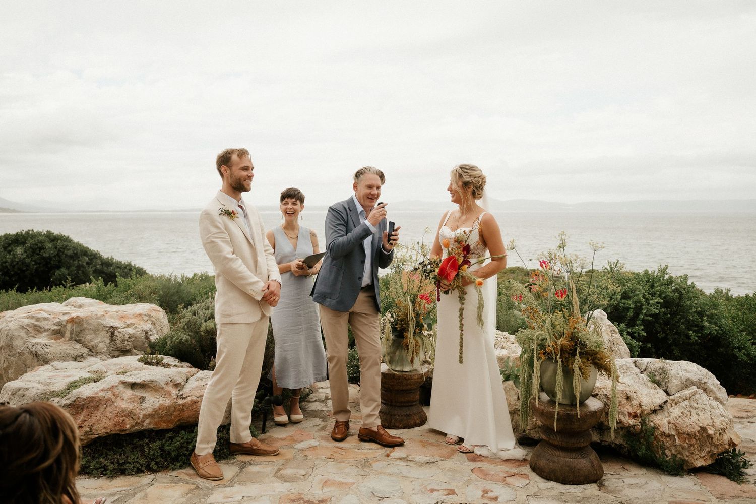 An intimate oceanside wedding ceremony takes place on a rocky cliff overlooking the sea.