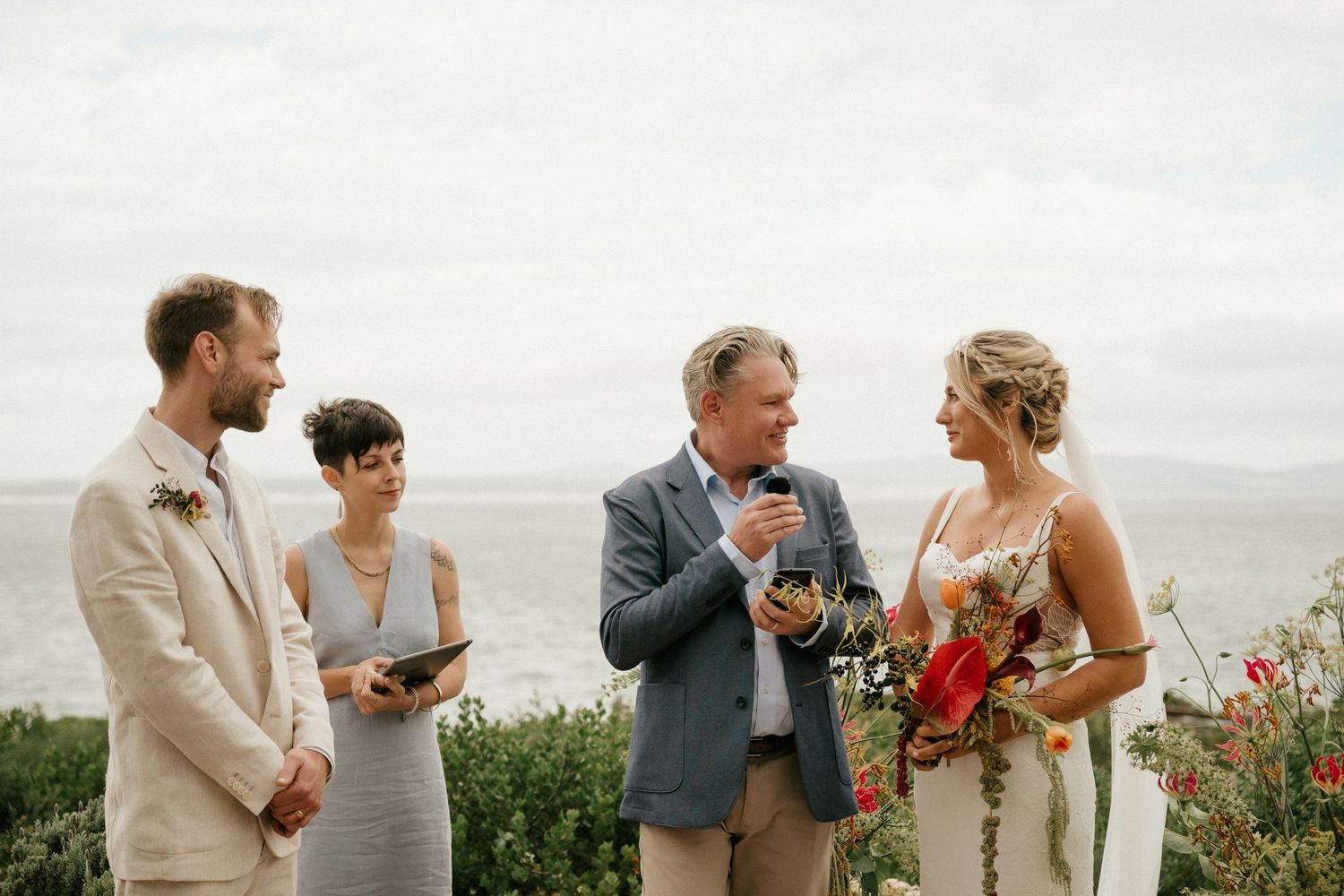 Intimate outdoor wedding ceremony by the ocean with colorful flowers and natural scenery.