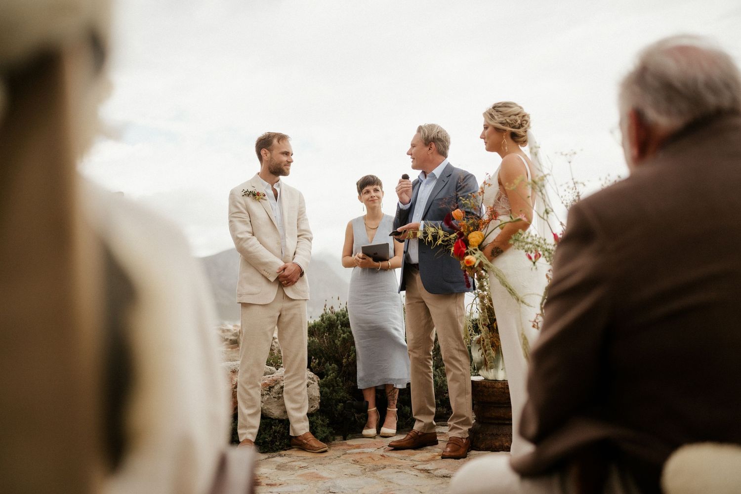 A wedding ceremony unfolds on a natural outdoor setting with guests observing the intimate moment.